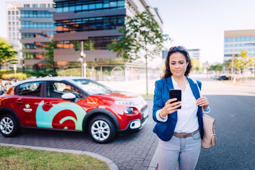 Frau nutzt Smartphone für Carsharing vor modernem Gebäude mit Smumo-Auto
