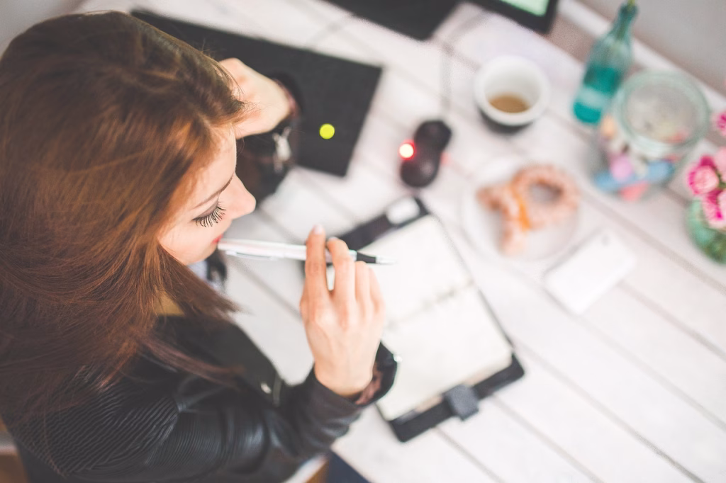 Studentin plant ihre Jobsuche am Schreibtisch mit Notizbuch, Laptop und Kaffee